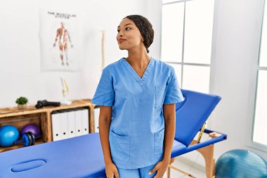 Güzel İspanyol fizyoterapist kadın acı dindirme kliniğinde yan yana gülümsüyor ve doğal bir ifade takınıyor. Kendinden emin gülen. 