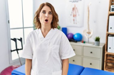 Orta yaşlı fizyoterapist kadın ağrı kesici kliniğinde çalışıyor. Şaşırmış ve korkmuş bir ifade, korku ve heyecanlı bir yüz ifadesi var.. 