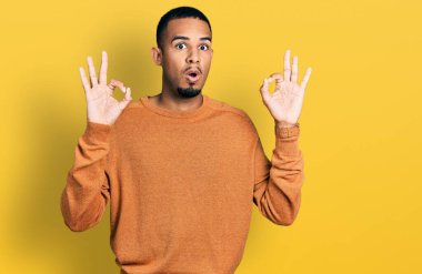 Gündelik giysiler giymiş genç Afro-Amerikan bir adam parmaklarıyla onay sembolü yaparken şaşırmış ve şok olmuş görünüyor. çılgın ifade 