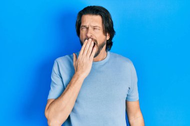 Orta yaşlı, günlük kıyafetler giyen beyaz bir adam ağzını eliyle kapatmaktan sıkılmış. Huzursuz ve uykulu.. 