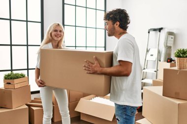 Genç ve güzel bir çift mutlu bir şekilde gülümsüyor. Yeni evlerinde büyük bir karton kutu tutuyorlar..