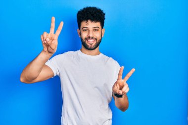 Sakallı, sıradan beyaz tişörtlü, dili dışarı fırlamış ve zafer işareti yapan genç bir Arap. İki numara.. 