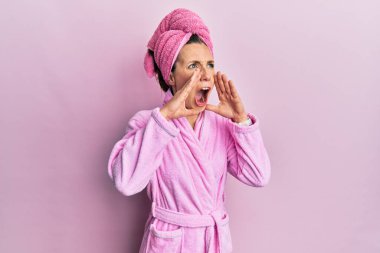 Duş başlığı ve bornoz takan genç sarışın kadın elleri ağızda bağırarak bağırıyor. 