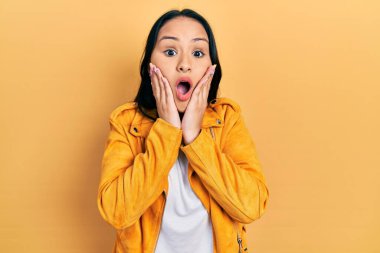 Burnu delinmiş, sarı deri ceketli, güzel İspanyol bir kadın. Korkmuş, şok olmuş, şaşırmış ve yüzünde elleri olan. 