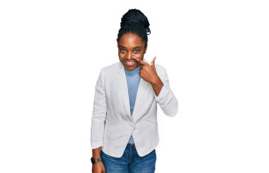 Genç Afro-Amerikan kadın iş kıyafetleri giyip, el ve burnu parmakla göstererek neşeli bir şekilde gülümsüyor. güzellik konsepti 
