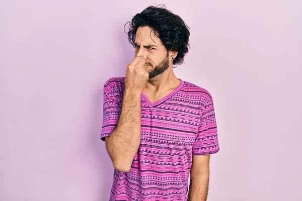 カジュアルなピンクのTシャツを着たハンサムなヒスパニック系の男性は 臭いと嫌な 耐えられない匂いを嗅ぎ 鼻の上に指で息を保持します 臭いが悪い — ストック写真