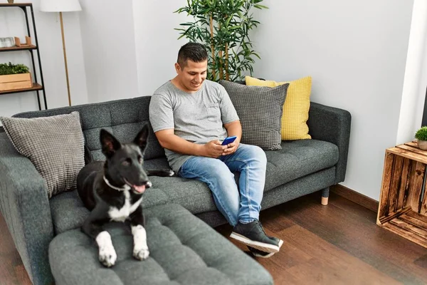 年轻的他的惊慌失措的男人用智能手机坐在沙发上 家里带着狗 — 图库照片