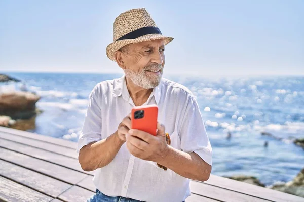 Senior Man Smiling Confident Wearing Summer Hat Using Smartphone Seaside — Stock Photo, Image