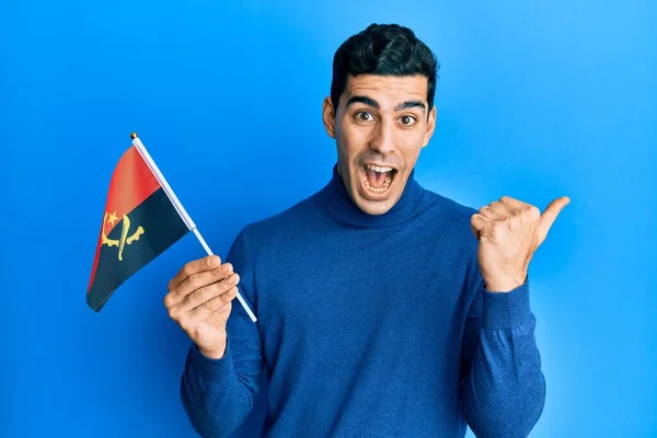 Pohledný Hispánec Držící Angolskou Vlajku Ukazující Palcem Nahoru Stranu Šťastně — Stock fotografie
