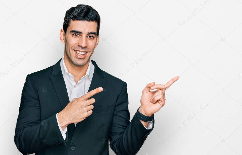 Handsome hispanic man wearing business clothes smiling and looking at the camera pointing with two hands and fingers to the side. 