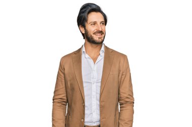 İş kıyafetleri giymiş genç İspanyol bir adam yüzünde gülümseme ve doğal bir ifadeyle yan yana bakıyor. Kendinden emin gülen. 