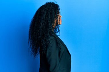 Orta yaşlı Afro-Amerikalı kadın, iş kıyafetleri içinde rahat bir görünüm takınıyor, doğal bir yüz ifadesi ve kendine güvenen bir gülümsemeyle poz veriyor.. 
