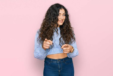 Günlük kıyafetler giyen genç İspanyol kız mutlu ve komik yüzüyle kamerayı işaret ediyor. iyi enerji ve titreşimler. 