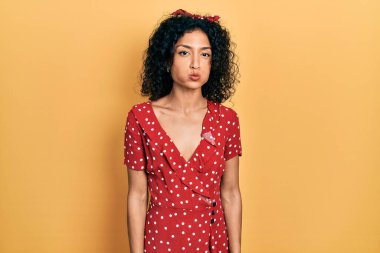 Yazlık elbise giyen, komik yüzlü, yanak şişiren genç Latin kız. Havayla şişmiş ağız, çılgın bir ifade.. 