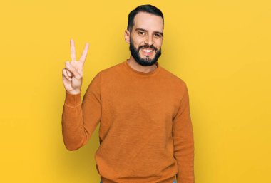 Sakallı, sıradan bir kazak giyen, gülümseyen ve kameraya bakıp zafer işareti yapan genç bir adam. İki numara.. 