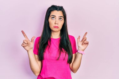 Gündelik pembe tişört giyen genç İspanyol kız üzgün ve üzgün görünüyor, parmaklarıyla yönü gösteriyor, mutsuz ve depresif.. 