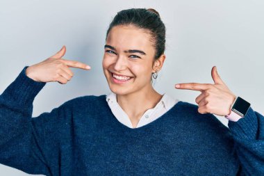 Günlük kıyafetler giyen, neşeli gülümseyen, parmaklarıyla ve ağzıyla işaret eden beyaz bir genç kız. diş sağlığı kavramı. 