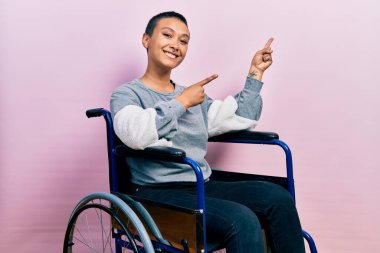 Tekerlekli sandalyede oturan, gülümseyen ve kameraya bakan, iki eli ve parmağı yanda olan güzel İspanyol kadın.. 