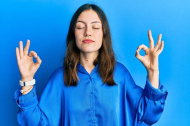 Mavi gömlekli genç esmer kadın rahatla ve gözleri kapalı gülümse parmaklarıyla meditasyon hareketi yapıyor. yoga konsepti. 