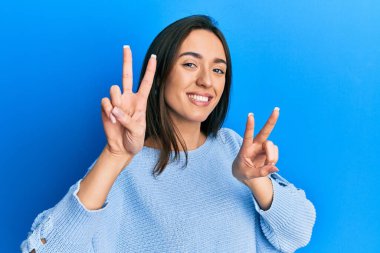 Gündelik kıyafetler giyen genç İspanyol kız kameraya bakıp zafer işareti yaparken parmaklarını gösteriyor. İki numara.. 