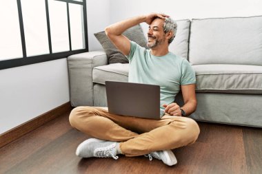 Orta yaşlı İspanyol bir adam oturma odasında dizüstü bilgisayar kullanıyor. Gülümsüyor, el hareketleriyle saçlara dokunuyor, çekici ve modaya uygun poz veriyor. 