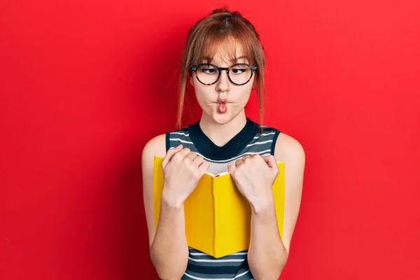 Redhead Young Woman Reading Book Wearing Glasses Making Fish Face — Stock Photo, Image