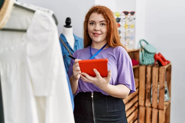 在服装店工作的红头发年轻女人用触摸板 — 图库照片