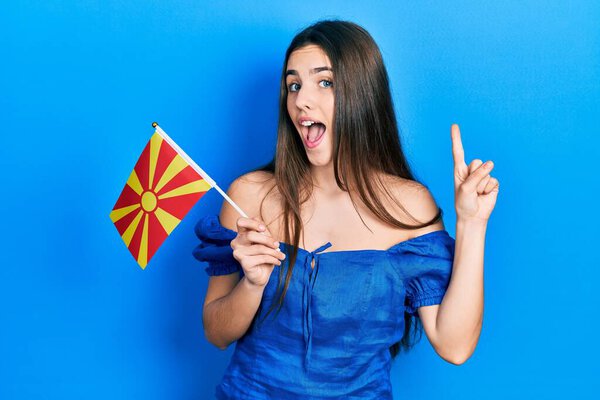 Молодая брюнетка-подросток с македонским флагом, улыбающаяся с идеей или вопросом, указывая пальцем со счастливым лицом, номер один 