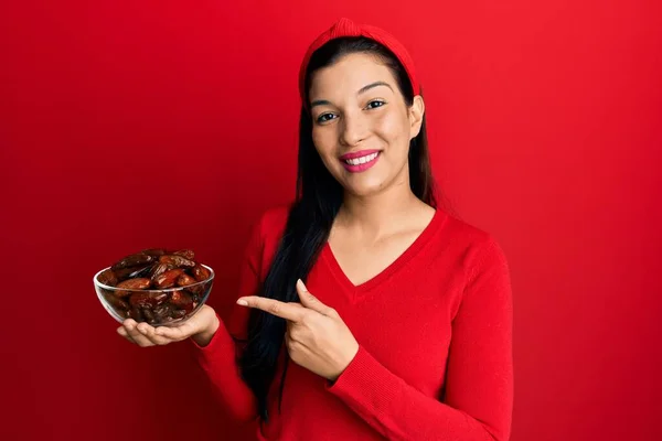 年轻的拉丁女人拿着盛有枣子的碗 开心地微笑着 手指手画脚 — 图库照片