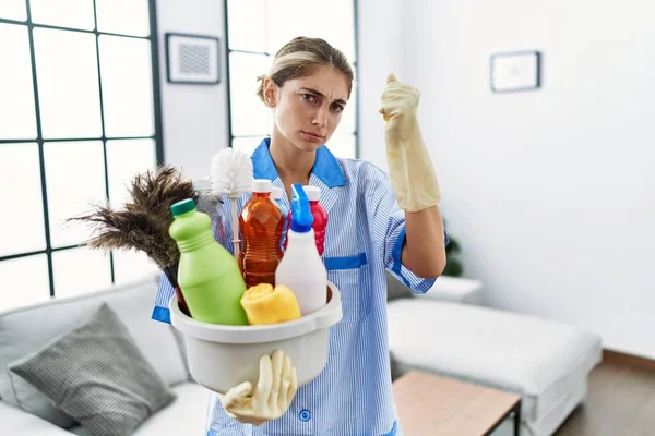 Jovem Loira Vestindo Uniforme Mais Limpo Segurando Produtos Limpeza Irritado — Fotografia de Stock