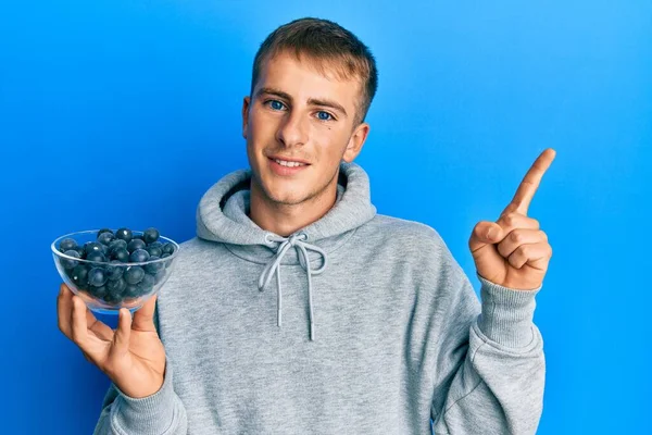 Jovem Caucasiano Segurando Tigela Mirtilos Sorrindo Feliz Apontando Com Mão — Fotografia de Stock