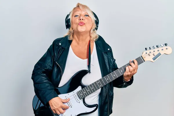 Blondynka Średnim Wieku Gra Gitarze Elektrycznej Pomocą Słuchawek Patrząc Aparat — Zdjęcie stockowe