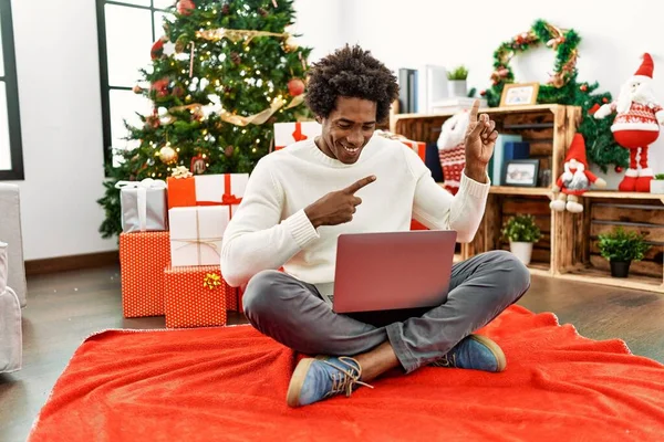 아프리카계 크리스마스 앉아서 노트북을 사용하고 웃으며 손가락으로 가리키고 카메라를 바라본다 — 스톡 사진