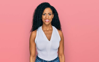 Orta yaşlı Afro-Amerikalı kadın kolsuz gömlekli, sıradan giyinmiş mutlu ve havalı bir gülümsemesi var. şanslı kişi. 