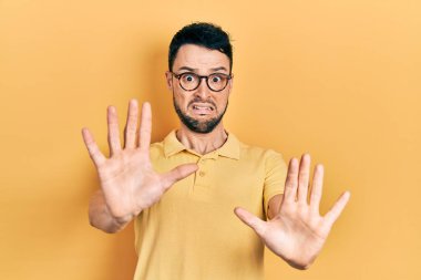 Günlük kıyafetler ve gözlük takan genç İspanyol adam korku ifadesinden korkmuş ve dehşete düşmüş. El kol hareketi yapmayı kes, şok içinde bağır. panik konsepti. 