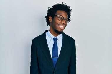 Genç Afro-Amerikalı takım elbiseli bir adam yüzünde gülümseme ve doğal bir ifadeyle yan yana bakıyor. Kendinden emin gülen. 