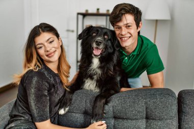 Genç, beyaz bir çift, mutlu bir şekilde gülümsüyor ve evde köpekleriyle koltukta oturuyor..