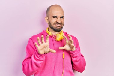 Spor kıyafetleri giyen ve kulaklık takan genç kel bir adam tiksindirici tepki verdiği için rahatsız ve korku dolu bir ifade takınıyor. Eller havada. 