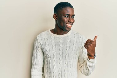 Genç Afro-Amerikalı günlük kıyafetler giymiş mutlu yüzüyle gülümseyen ve başparmağıyla yüzünü gösteren bir adam.. 