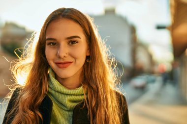 Genç sarışın kız gülümsüyor, mutlu bir şekilde şehirde duruyor..
