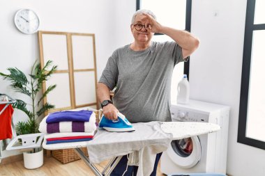 Kıdemli beyaz adam evde ütü yapıyor. Gülümsüyor. Mutluluktan gülümsüyor. 