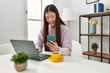 Laptop ve akıllı telefon kullanan Çinli genç bir kız evdeki masada oturuyor..