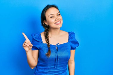 Gündelik giysiler giyen genç İspanyol kız bir numarayı gösterip işaret ederken kendinden emin ve mutlu bir şekilde gülümsüyor.. 