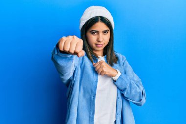 Tatlı yün şapkalı genç Latin kadın dövüşmek için yumruk atıyor, agresif ve öfkeli saldırı, tehdit ve şiddet 