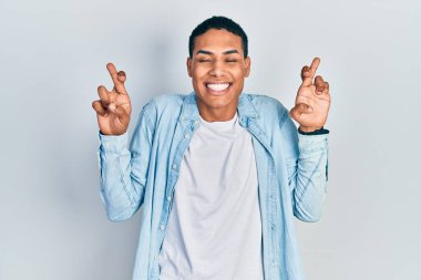 Afro-Amerikan genç adam günlük kıyafetler giyip umut ve gözlerin kapalı bir şekilde gülümseyerek el işareti yapıyor. Şans ve batıl inançlar. 