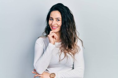 Gündelik kıyafetler giyen genç İspanyol kadın kameraya kollarını kavuşturmuş ve çenesi üzerinde kendinden emin bir şekilde bakıyor. Olumlu düşünmek. 
