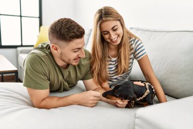 Genç İspanyol çift evde köpekle kanepede mutlu bir şekilde yatıyor..