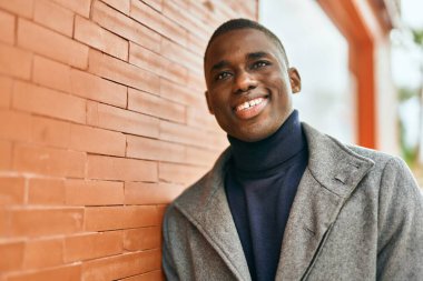 Genç Afrikalı Amerikalı adam gülümseyerek şehirde mutlu mesut duruyor.