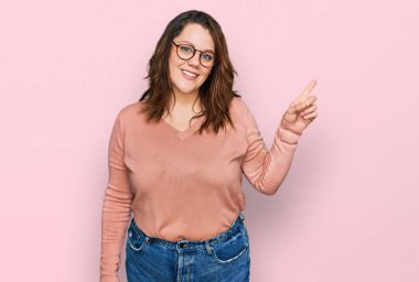 Genç ve cüsseli bir kadın. Günlük kıyafetler ve gözlük takıyor. Yüzünde kocaman bir gülümseme var.. 