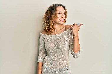 Gündelik giysiler giymiş genç beyaz bir kadın baş parmağını yukarı kaldırıyor ve ağzı açık gülümsüyor. 